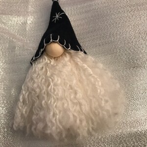 May include: A small white gnome ornament with a black felt hat and a white star design. The gnome has a white fluffy beard.