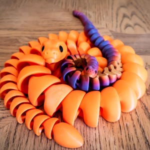 May include: A coiled orange and purple snake toy made of plastic. The snake is curled up in a spiral shape, with the head of the snake at the top of the coil.