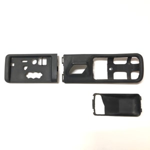 May include: Three black plastic pieces for a car door panel. The pieces are rectangular and have various cutouts and holes.