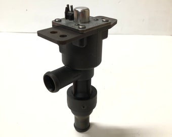 May include: A black automotive coolant control valve featuring a cylindrical body with two hose connection ports, a metallic top plate with a central silver-coloured plunger, and a mounting flange with two circular holes for secure installation.