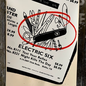 Puede incluir: Una ilustración en blanco y negro de una navaja multiusos con un círculo rojo alrededor. El texto "ELECTRIC SIX" está en blanco y negro con las palabras "Test Your Reflex" y "Night Kills The Day" en una fuente más pequeña. El texto "4.14.2007 Club Dada Dallas, TX" también está incluido.