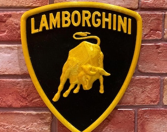 Puede incluir: Un logotipo de Lamborghini negro y amarillo con la palabra "Lamborghini" en letras amarillas y un toro cargando en amarillo.