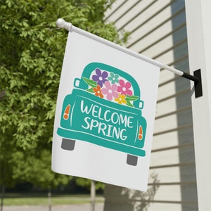 May include: A teal blue pickup truck with a white "Welcome Spring" message on the back. The truck bed is filled with colorful flowers.