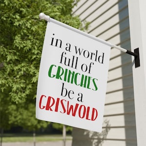 May include: White flag with the text "in a world full of GRINCHES be a GRISWOLD" in black, green, and red lettering.