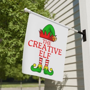 May include: A white Christmas flag with a green and red elf illustration. The text on the flag reads "The Creative Elf".