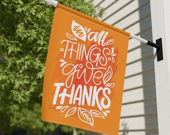 May include: Orange garden flag with white text that reads "In all things give thanks" with a leafy design.