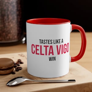 May include: White ceramic coffee mug with a red rim and handle. The mug has the text "Tastes like a Celta Vigo win" printed on it in black and red.