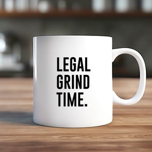 Può includere: Tazza da caffè in ceramica bianca con testo nero che recita "LEGAL GRIND TIME."