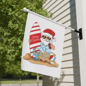 Pode incluir: Uma bandeira branca com um desenho animado do Papai Noel usando óculos de sol e uma camisa havaiana, segurando uma prancha de surf e uma bebida. O texto "Merry Christmas" está na prancha de surf.
