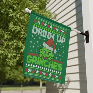 Könnte beinhalten: Grüne Weihnachtsflagge mit einem Grinch, der einen Weihnachtsmann-Hut trägt und den Text "Drink Up Grinches".
