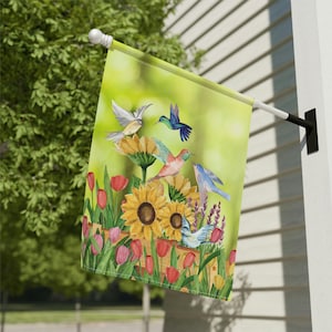 May include: A colourful garden flag with a watercolour design of hummingbirds and sunflowers. The flag features a variety of colours, including green, yellow, blue, red and pink.