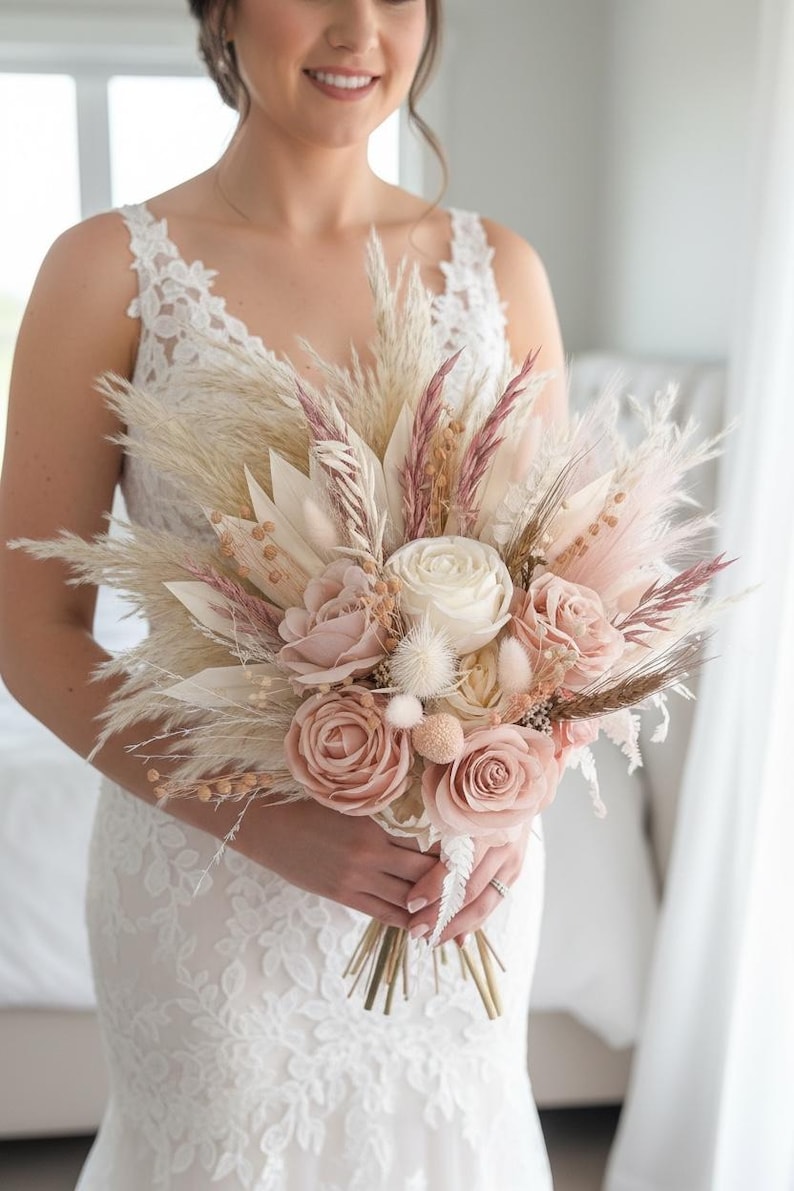 May include: A bridal bouquet featuring a mix of dried and faux flowers in soft pink, cream, and beige tones. The arrangement includes roses, pampas grass, and other textured elements, held together with gold-toned stems.