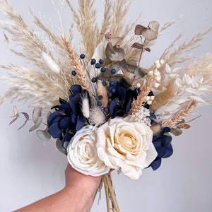 May include: A dried flower bouquet featuring white pampas grass, blue hydrangeas, white roses, and eucalyptus sprigs.
