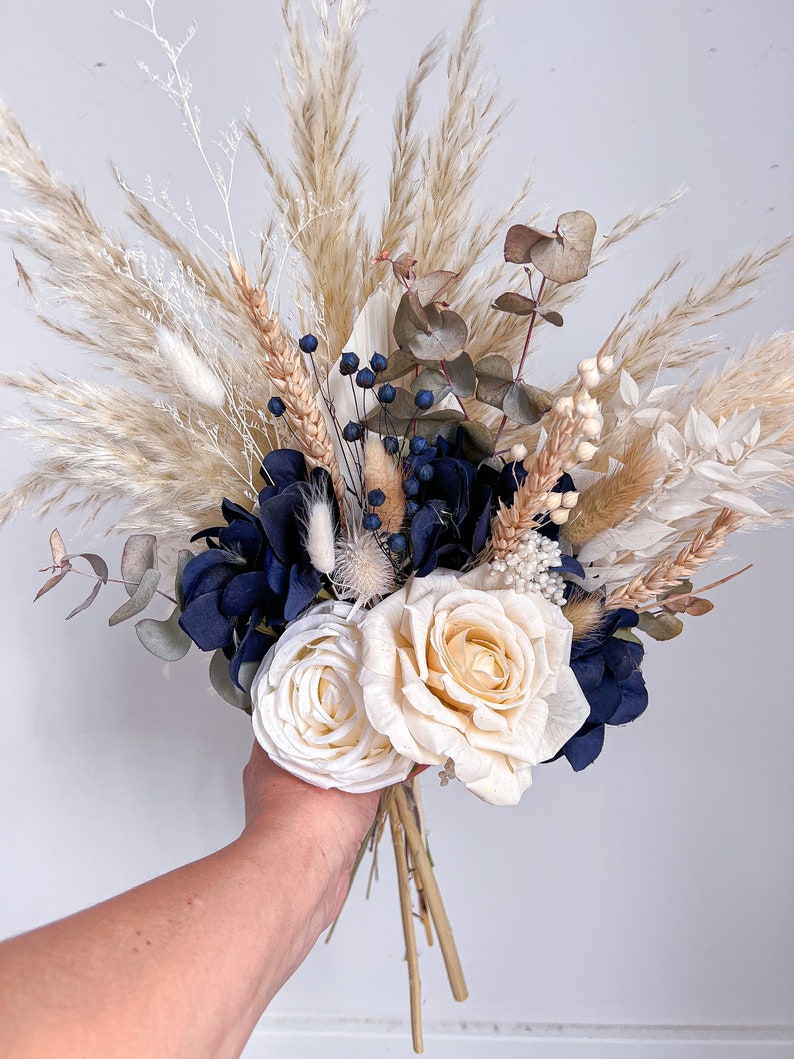 May include: A dried flower bouquet featuring white pampas grass, blue hydrangeas, white roses, and eucalyptus sprigs.