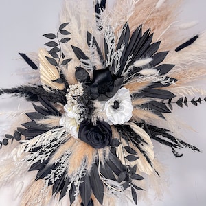 May include: A black and white dried flower arrangement with pampas grass, black palm leaves, and white and black flowers.