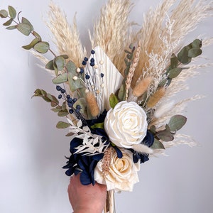 May include: A bouquet of dried flowers featuring white roses, blue hydrangeas, pampas grass, and eucalyptus.
