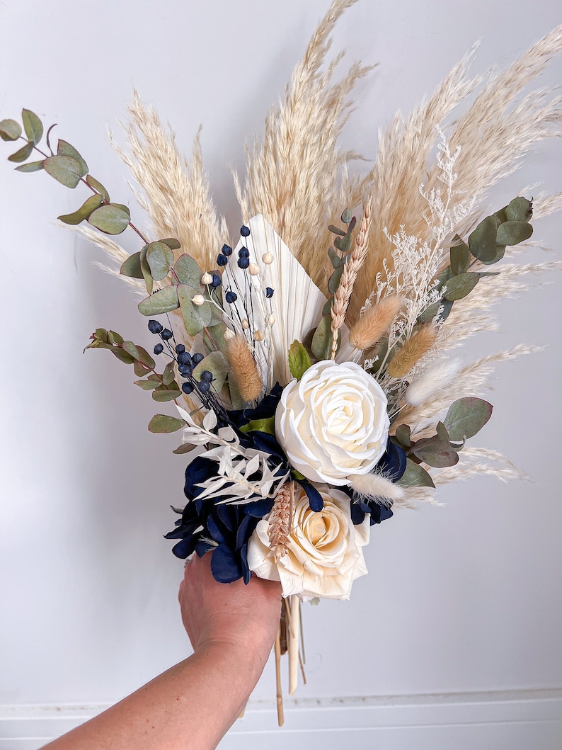 May include: A bouquet of dried flowers featuring white roses, blue hydrangeas, pampas grass, and eucalyptus.