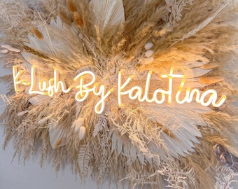 May include: A neon sign with the text "K-Lush By Kalotina" surrounded by dried pampas grass and other dried flowers.