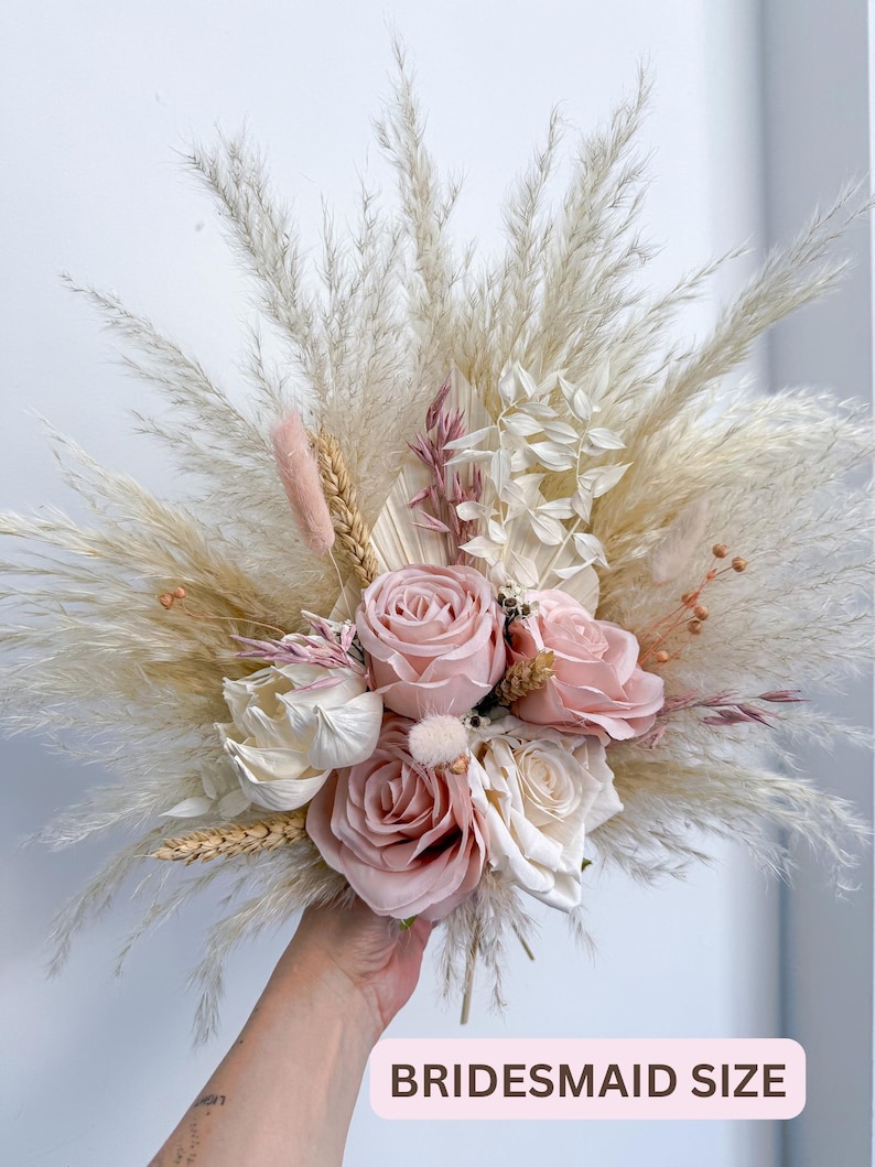 May include: A bridesmaid-sized bouquet featuring a mix of dried pampas grass, wheat, and faux roses in shades of pink and cream. The bouquet includes the text "BRIDESMAID SIZE".