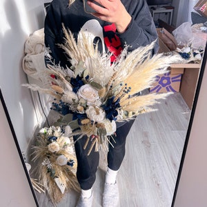 May include: A bouquet of dried flowers with white and cream coloured flowers, blue berries, and tan pampas grass.