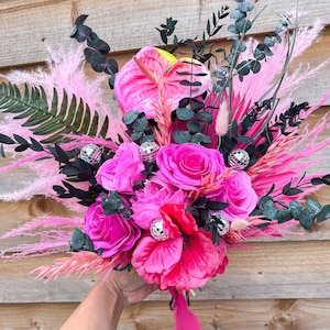 May include: A pink and green bouquet of flowers with disco ball accents. The bouquet includes pink roses, pink anthurium, pink pampas grass, and eucalyptus.