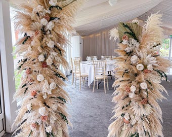 Arranjo de flores secas para casamento com arco quebrado, painel de fundo com pilares da Pampa, arranjos florais para cerimônia em colunas.