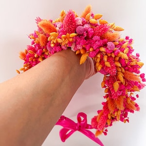 May include: A pink and orange floral crown with a pink ribbon tied at the bottom.