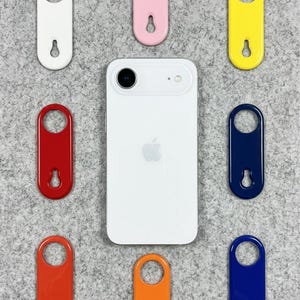 May include: A white smartphone is surrounded by eight colorful, oval-shaped keychains in white, pink, yellow, red, orange, and two shades of blue. The keychains have a circular top and a teardrop-shaped opening at the bottom.