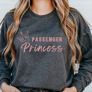 May include: Dark heather grey sweatshirt with a pink crown and the text "Passenger Princess" in pink.