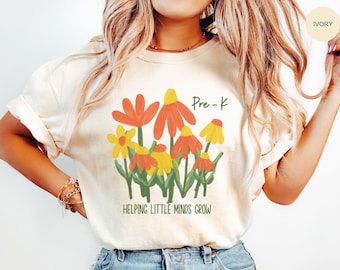 Puede incluir: Una camiseta blanca con un diseño floral y el texto "Pre-K Helping Little Minds Grow".