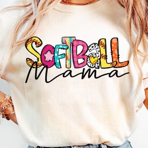 K&ouml;nnte beinhalten: Ein wei&szlig;es T-Shirt mit dem Schriftzug "Softball Mama" in bunten, verspielten Buchstaben. Die Buchstaben sind mit Baseballn&auml;hten, Sternen und Herzen verziert.