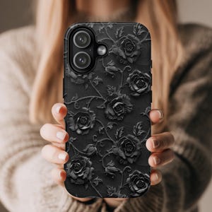 May include: Black phone case with a raised floral rose design. The case features a matte finish and a detailed pattern of roses and vines. The phone case has a dual-lens camera cutout.