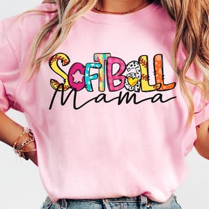 K&ouml;nnte beinhalten: Pinkes T-Shirt mit einer bunten Grafik, auf der "Softball Mama" steht.