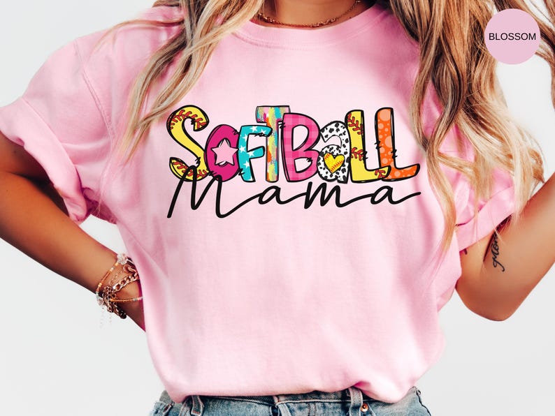 K&ouml;nnte beinhalten: Pinkes T-Shirt mit einer bunten Grafik, auf der "Softball Mama" steht.