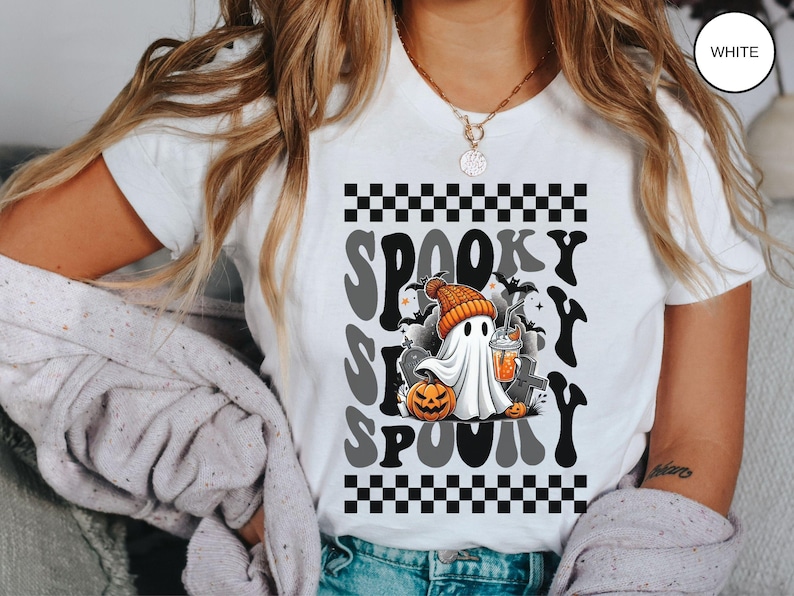 May include: White t-shirt with a black and white checkered pattern and the text "Spooky S-P-O-O-K-Y" in a retro font. A cartoon ghost wearing a hat and holding a pumpkin and a drink is in the center of the design.