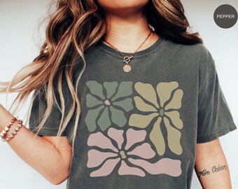 May include: Dark gray t-shirt featuring a floral design in muted green, tan, and pink. The shirt has a relaxed fit and a crew neck. The word "Pepper" is in a circle in the upper right corner.