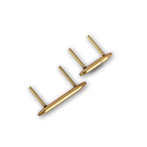 Może przedstawiać: Dwa zestawy złotych metalowych spinek do mankietów. Każda spinka do mankietów ma prostokątny pasek z dwoma pionowymi słupkami. Spinki do mankietów są wyświetlane na białym tle.