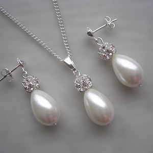 May include: A silver necklace and earring set. The necklace has a fine chain with a pendant featuring a cluster of small, sparkling crystals above a large, pear-shaped white pearl. The earrings match the pendant design.