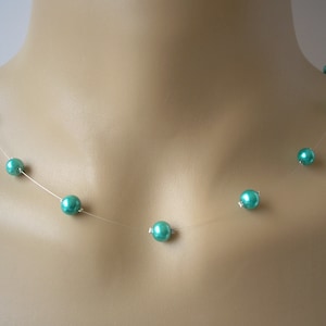 以下が含まれることがあります： 複数の丸いビーズが付いた、ターコイズ色のフローティングネックレス。ビーズはほぼ見えない糸に沿って均等に配置されており、繊細でエレガントな外観を作り出しています。ネックレスはマネキンに展示されています。