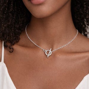 Collana girocollo con chiusura a T frontale, con grande cerchio e barretta argentati e chiusura a moschettone, su catena a maglie in acciaio inossidabile placcato argento per donna.