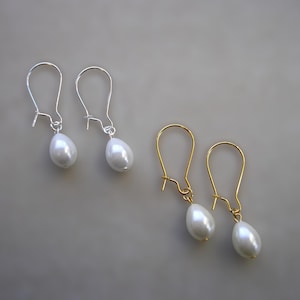 May include: Two pairs of teardrop pearl earrings. One pair has silver hooks, the other gold-coloured hooks. The pearls are white with a smooth, glossy finish. The earrings are displayed against a neutral grey background.