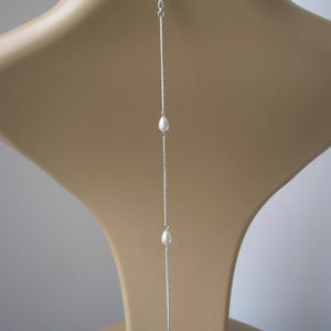May include: A silver necklace with three white teardrop-shaped pearls. The necklace hangs vertically, with the pearls spaced along a delicate chain. The clasp is visible at the top, and the necklace is displayed on a mannequin.