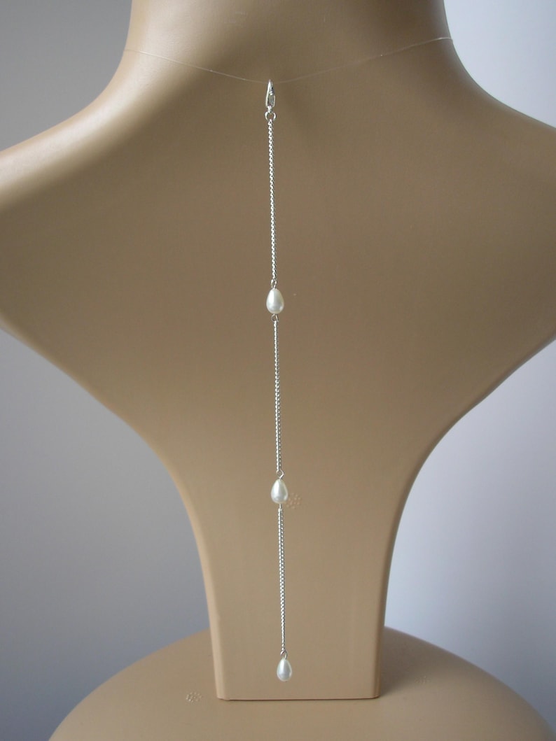 May include: A silver necklace with three white teardrop-shaped pearls. The necklace hangs vertically, with the pearls spaced along a delicate chain. The clasp is visible at the top, and the necklace is displayed on a mannequin.