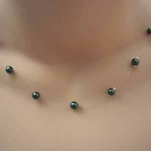 Può includere: Una delicata collana con perline verde scuro infilate su un filo quasi invisibile. Le perline sono uniformemente distanziate, creando un effetto fluttuante. La collana è un gioiello semplice ma elegante.