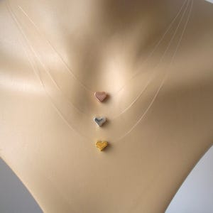 May include: A layered necklace with three heart-shaped charms in gold, silver, and rose gold.