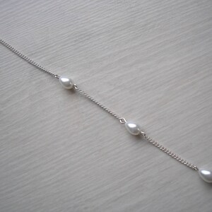 May include: A delicate silver chain bracelet featuring three teardrop-shaped pearls. The bracelet has a lobster clasp closure and is displayed on a light-colored surface. The pearls are evenly spaced along the chain.