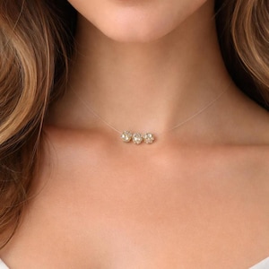 May include: A delicate necklace featuring a thin, transparent nylon cord strung with three small, round, sparkling clear crystal beads arranged horizontally in the center, creating a floating effect against the skin.