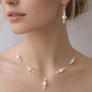 May include: A necklace and matching drop earring set featuring white faux pearls and clear faceted crystal beads strung on a thin, transparent nylon cord. The necklace has a central pearl drop, while the earring features a single pearl drop.