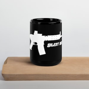 May include: Black coffee mug featuring a white silhouette of a rifle and the text "SILENT BUT DEADLY" printed on it.