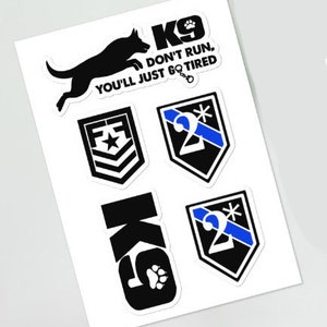 Peut inclure: Un ensemble de six autocollants noirs et blancs représentant une silhouette de chien, le texte "K9 Don't Run, You'll Just Go Tired", une empreinte de patte et le chiffre "2" avec une bande bleue.